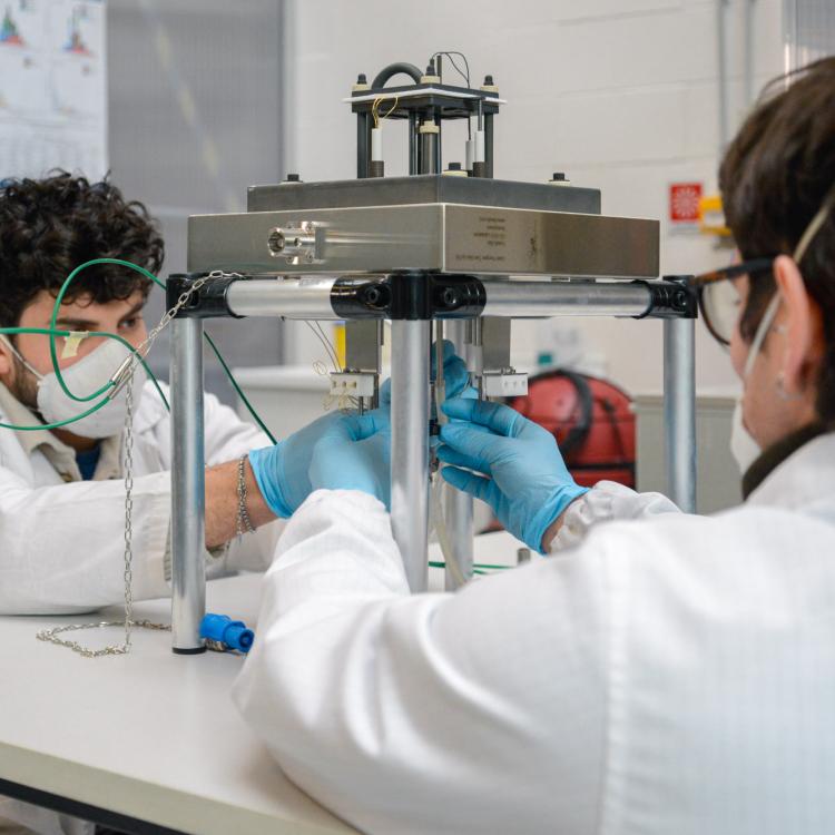 Two researchers in white lab coats and protective masks assembling scientific equipment on a table.